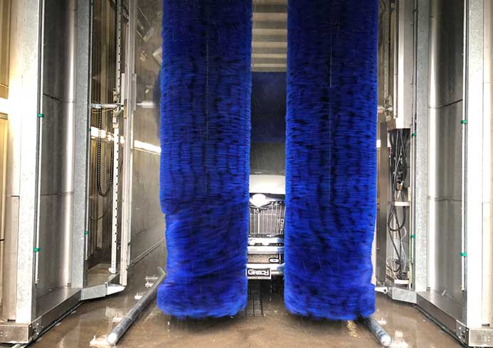 A small transit vehicle being washed by a bus wash system.